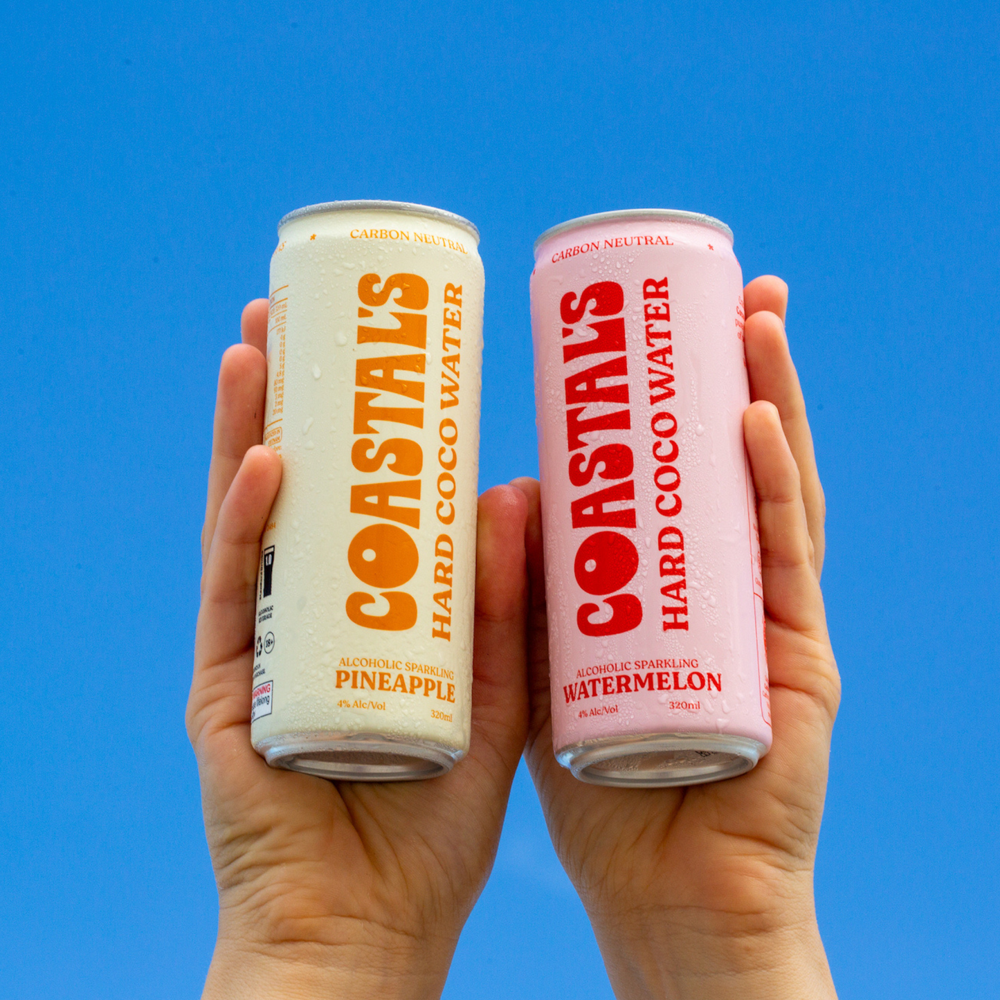 Two cans of Coastals Hard Coconut Water held against a blue sky.