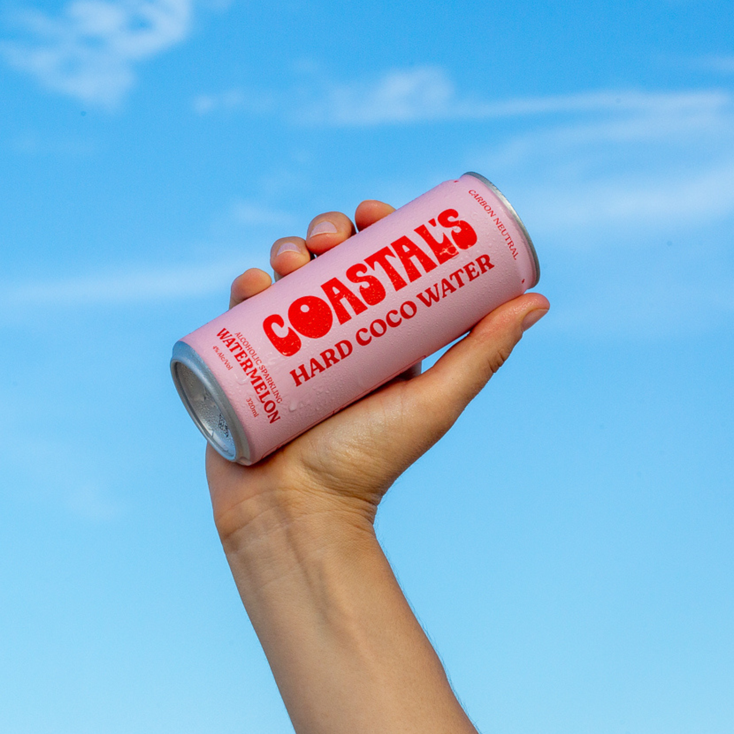 Hand holding a pink can of Coastals Hard Coconut Water in Watermelon flavour against a blue sky