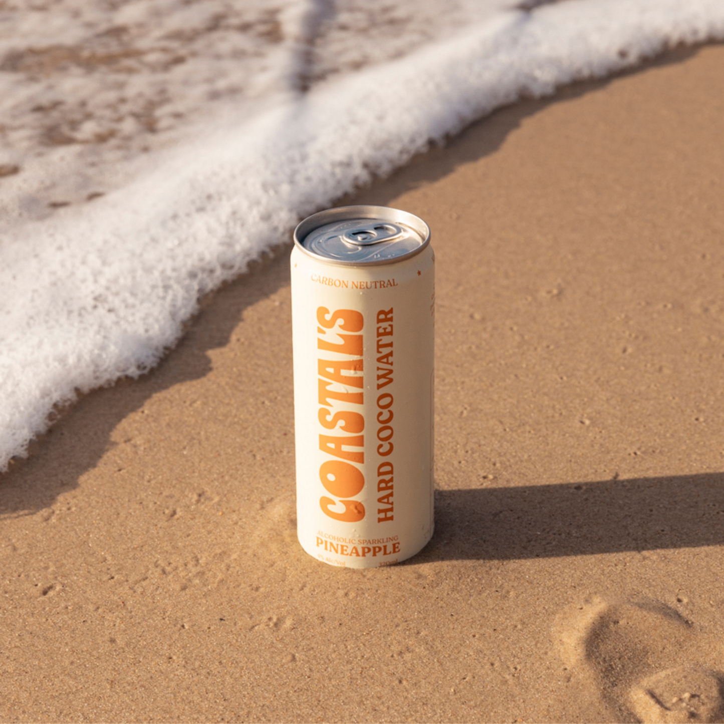 A can of Coastals Pineapple Sparkling Alcoholic Coconut Water with vodka and real pineapple juice by a wave at the beach.