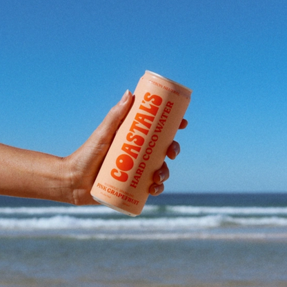 Hand holding a can of Coastals Hard Coconut water against a beach background
